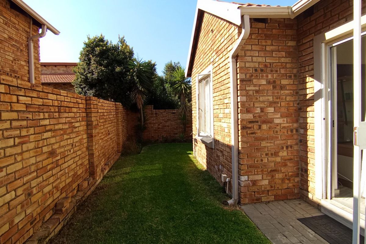 A private rear garden area featuring a well-maintained lawn, face brick boundary walls, and a paved walkway leading to the townhouse entrance.