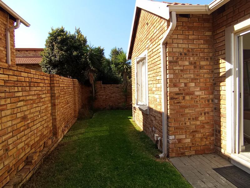 A private rear garden area featuring a well-maintained lawn, face brick boundary walls, and a paved walkway leading to the townhouse entrance.