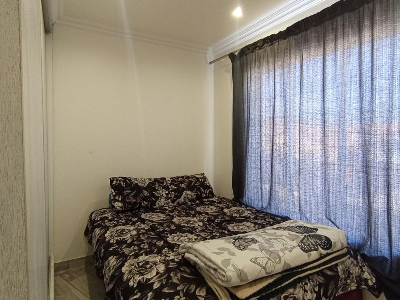 A compact bedroom featuring built-in cupboards, tiled flooring, and recessed downlighting, providing a functional and neutral space.