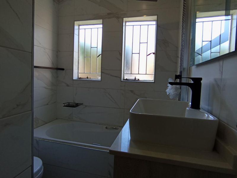 Modern bathroom featuring a built-in bathtub, vessel sink with black faucet, and elegant marble-look wall tiling.