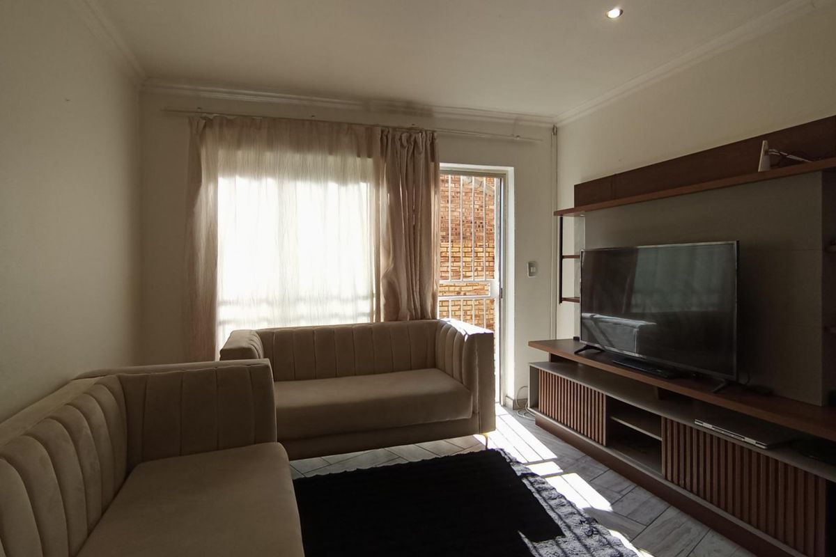 A living room featuring a built-in media unit, tiled flooring, and access to an outdoor area through a sliding glass door.