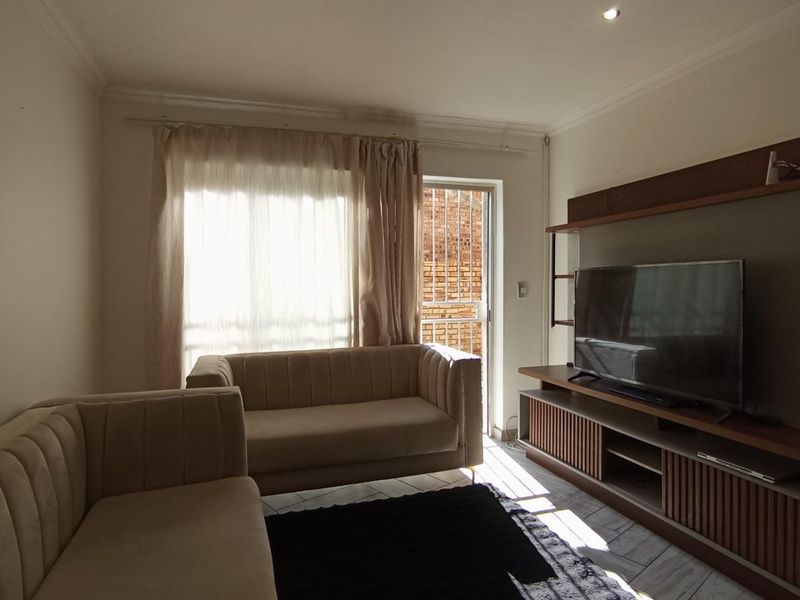 A living room featuring a built-in media unit, tiled flooring, and access to an outdoor area through a sliding glass door.