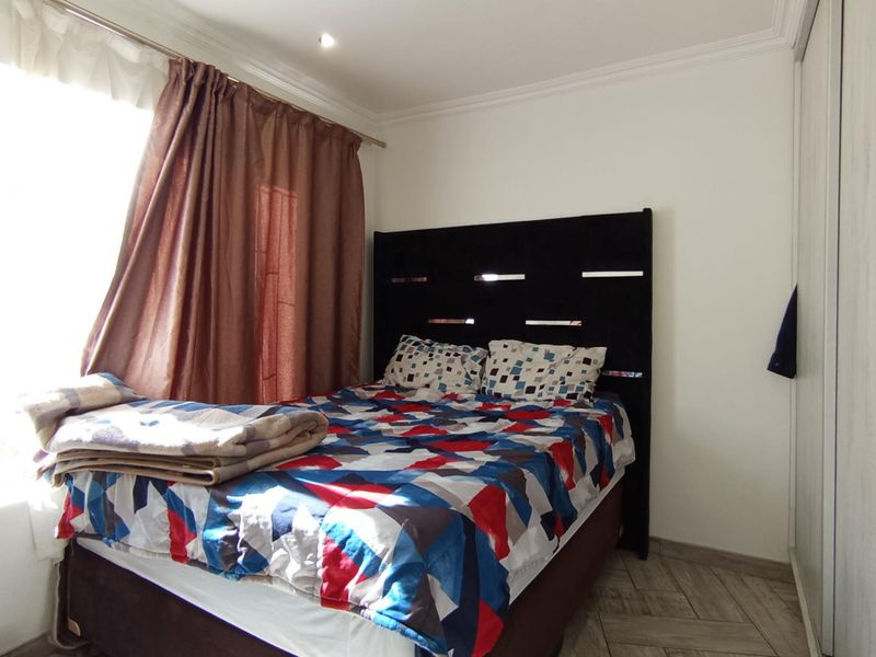 A functional bedroom featuring tiled flooring, built-in cupboards, and recessed downlighting, offering a clean and neutral space for personalization.