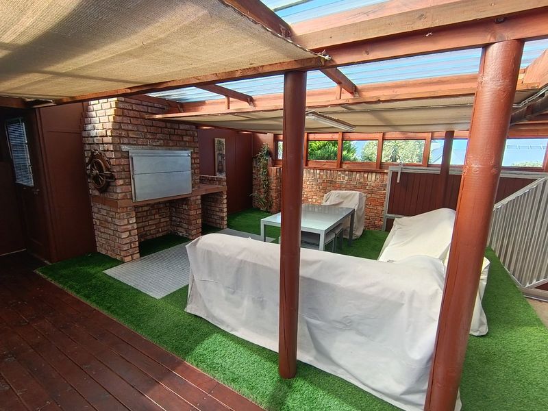 Covered outdoor patio featuring a built-in brick braai, timber pergola structure, and artificial grass flooring, ideal for relaxed outdoor entertaining.