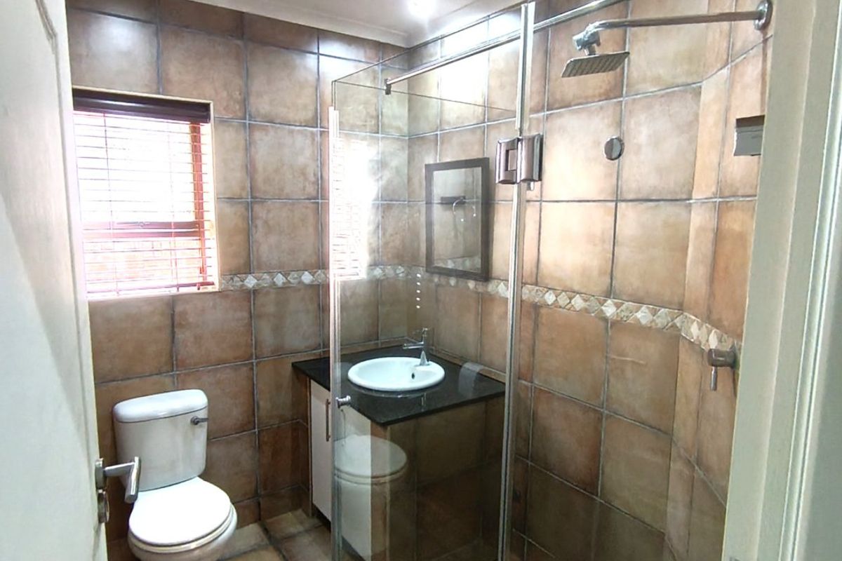 A functional bathroom featuring a glass-enclosed shower with a rain shower head, a vanity with a granite countertop, and full-height wall tiling.