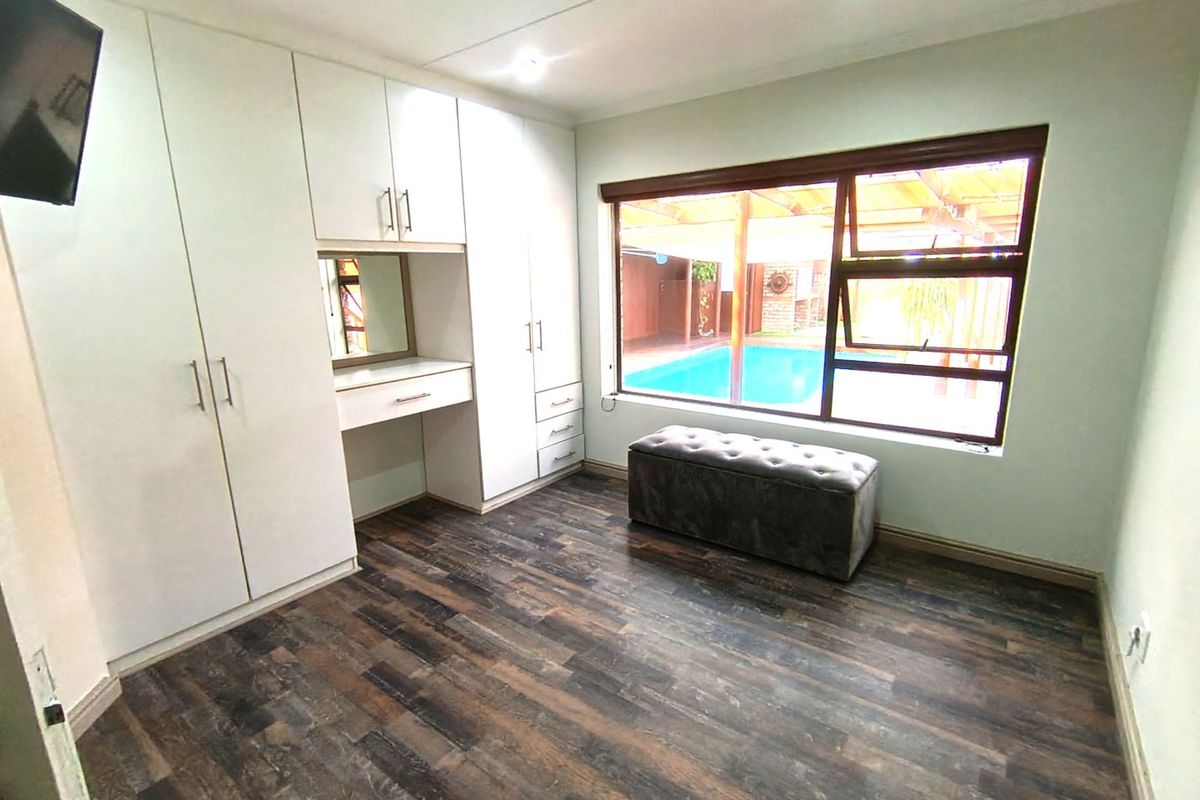 A well-maintained bedroom featuring built-in cupboards with an integrated vanity, dark laminate flooring, and a large window overlooking the pool area.