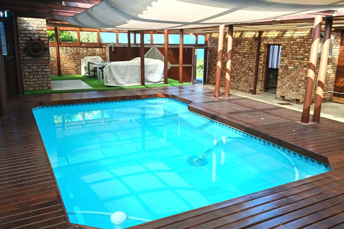 Covered outdoor pool area featuring timber decking, exposed brick walls, and a shade sail, providing a sheltered space for swimming and relaxation.