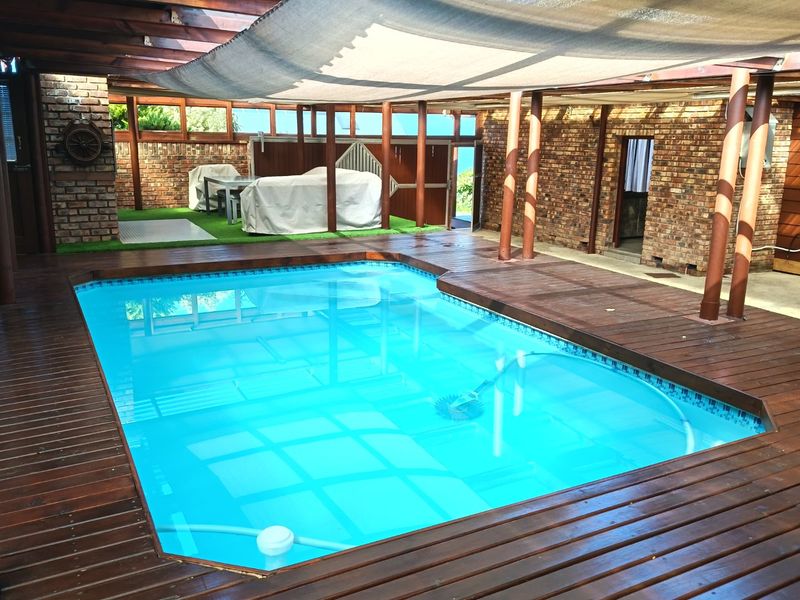 Covered outdoor pool area featuring timber decking, exposed brick walls, and a shade sail, providing a sheltered space for swimming and relaxation.