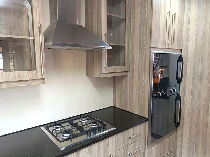 Modern kitchen featuring wood-grain cabinetry, granite countertops, a built-in oven, and a stainless steel gas hob with an integrated extractor fan.