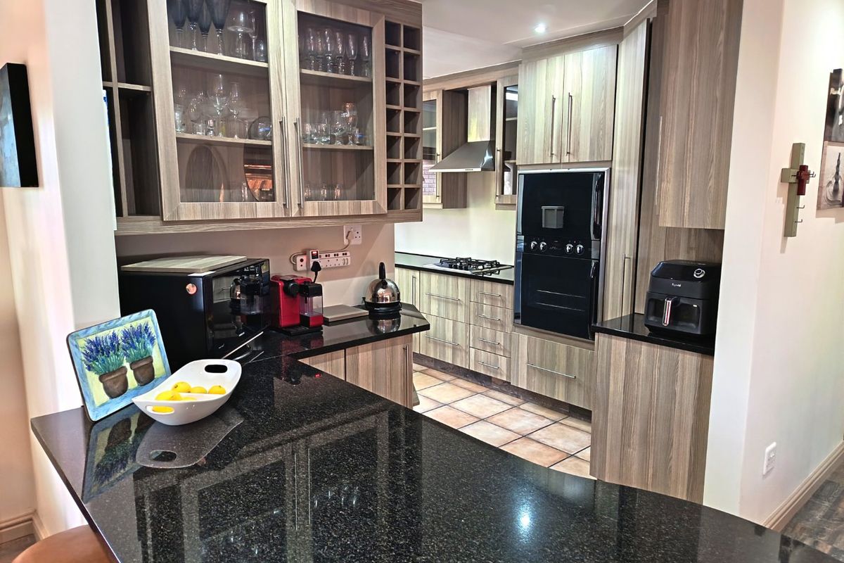 Modern kitchen featuring granite countertops, built-in oven, gas hob, extractor fan, and ample wood-finish cabinetry with glass display sections.