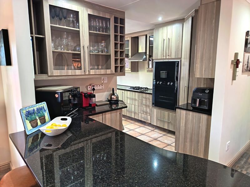 Modern kitchen featuring granite countertops, built-in oven, gas hob, extractor fan, and ample wood-finish cabinetry with glass display sections.