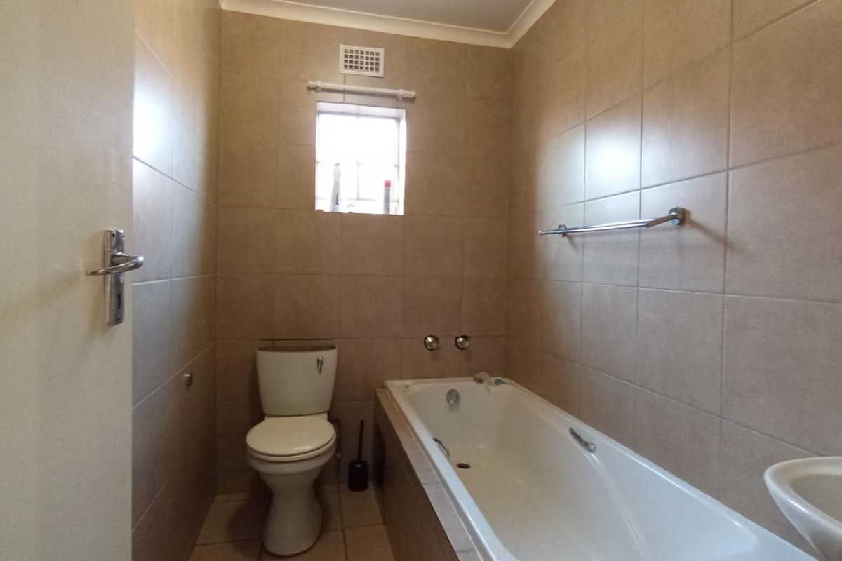 A functional bathroom featuring full-height wall tiling, a built-in bathtub, a standard toilet, and a wall-mounted basin.