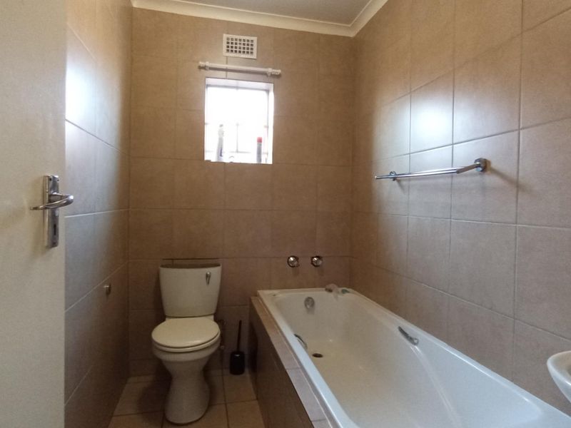 A functional bathroom featuring full-height wall tiling, a built-in bathtub, a standard toilet, and a wall-mounted basin.