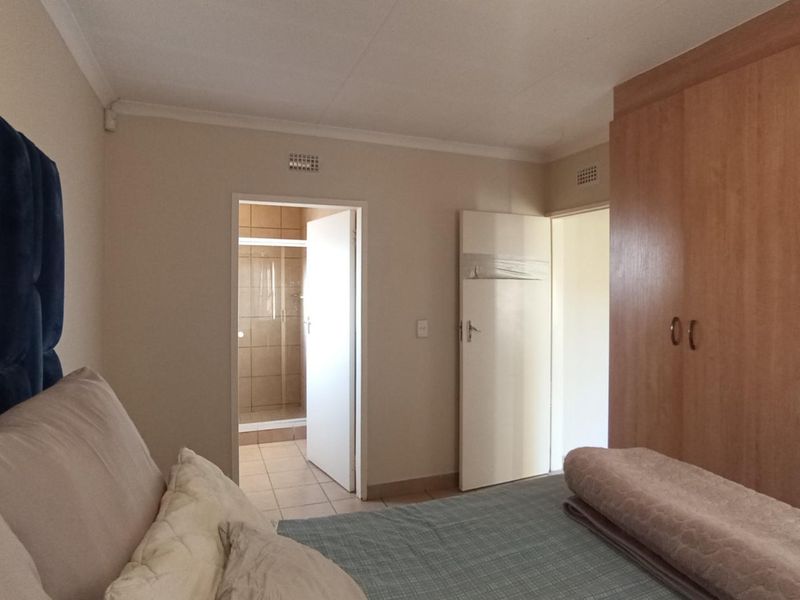 A bedroom featuring built-in wooden wardrobes and an adjoining en-suite bathroom with tiled finishes.