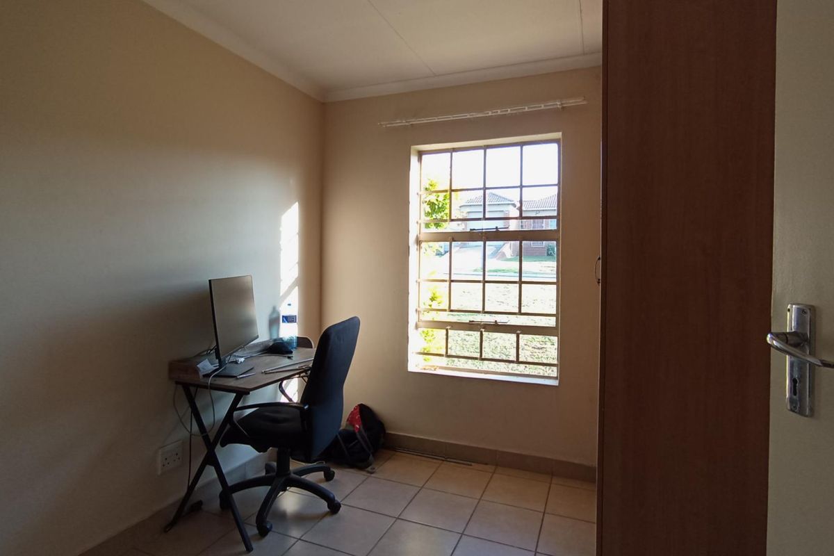 A functional bedroom featuring tiled flooring, a window with security bars, and a built-in cupboard, suitable for use as a bedroom or home office.