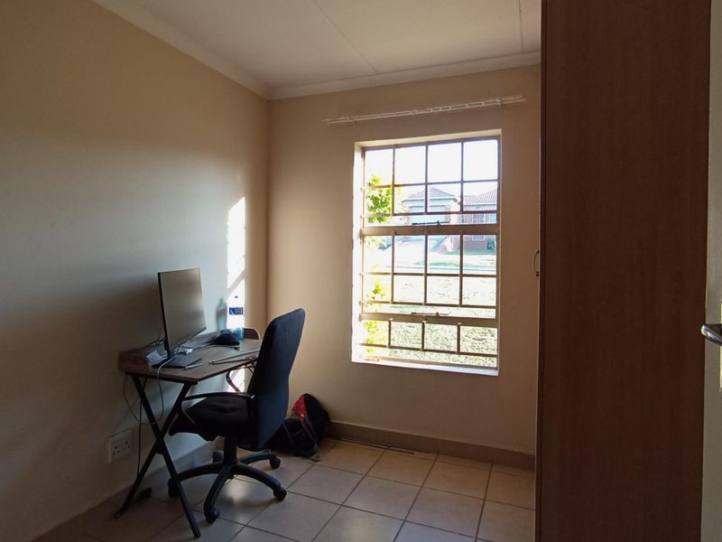 A functional bedroom featuring tiled flooring, a window with security bars, and a built-in cupboard, suitable for use as a bedroom or home office.
