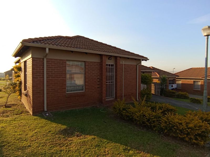 A well-maintained face brick house featuring a tiled roof, security gate, and paved driveway, situated in a neat residential estate setting.