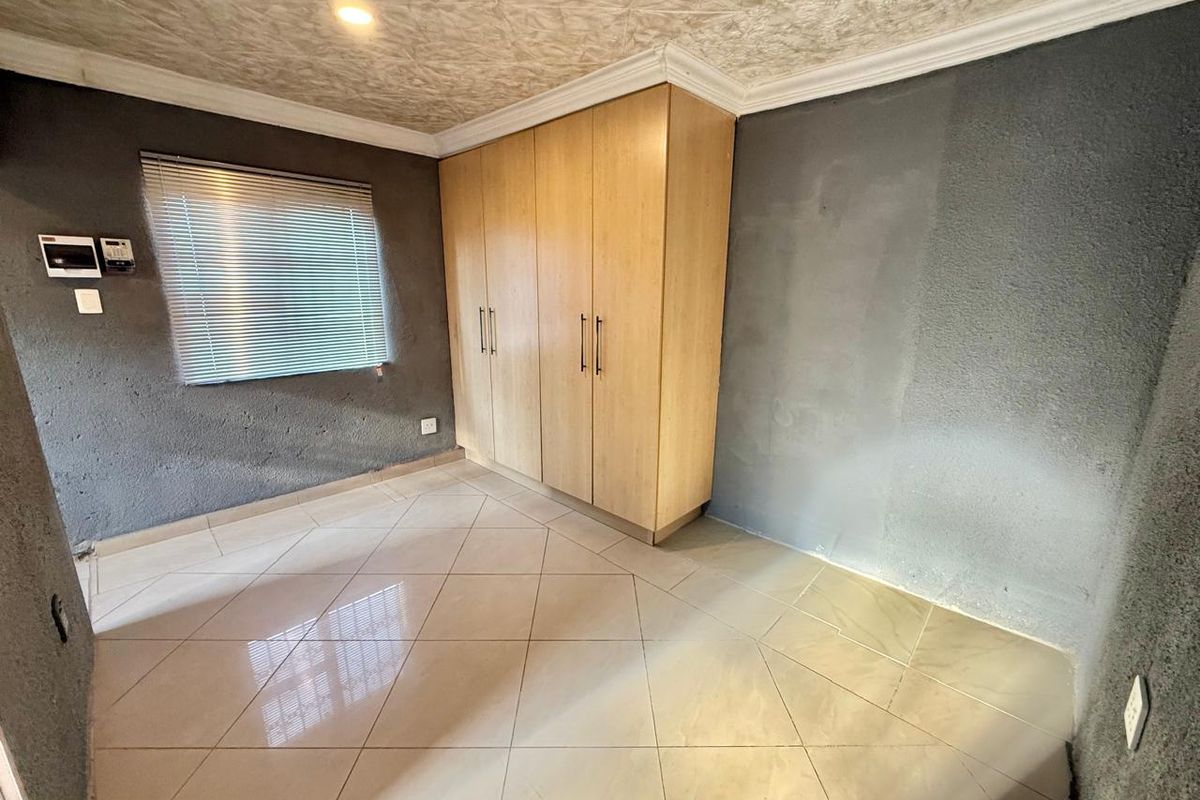 A vacant bedroom featuring built-in wooden cupboards, tiled flooring, and textured walls with venetian blinds.