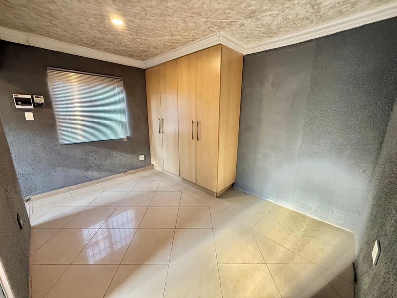 A vacant bedroom featuring built-in wooden cupboards, tiled flooring, and textured walls with venetian blinds.