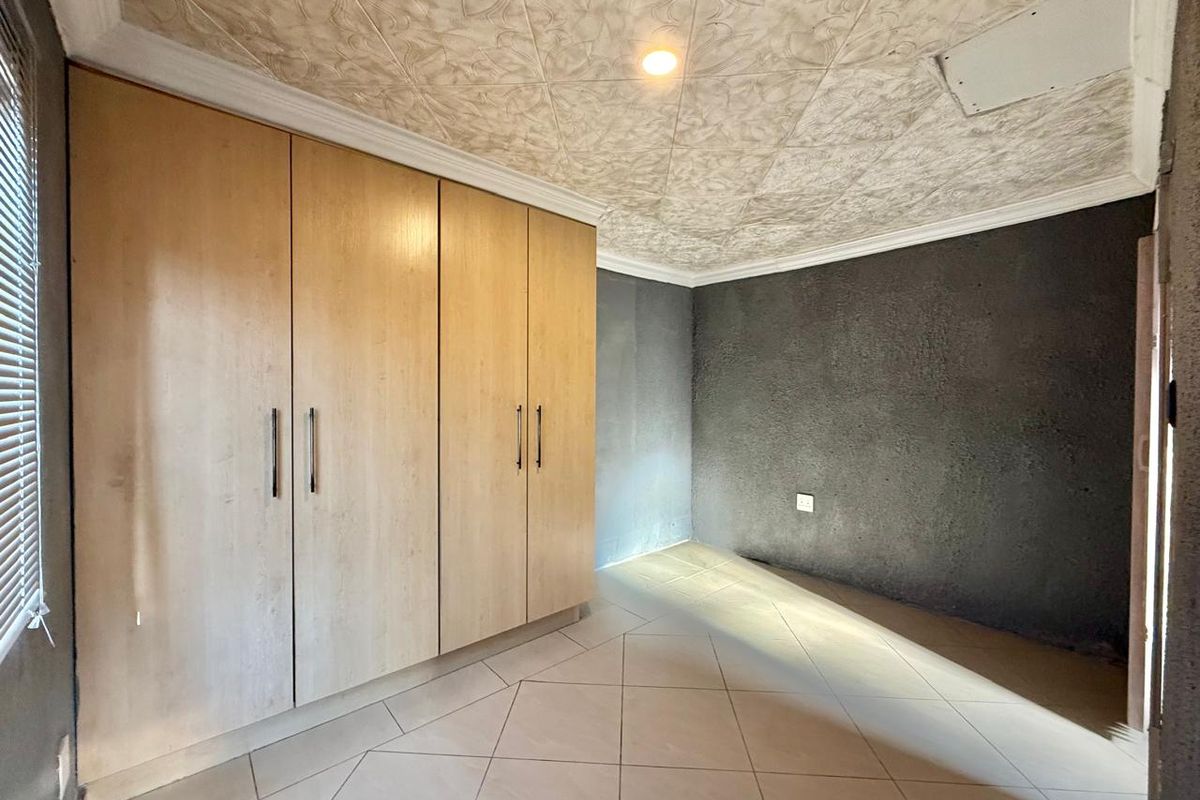 A vacant bedroom featuring built-in wooden cupboards, tiled flooring, and a decorative textured ceiling with coving.