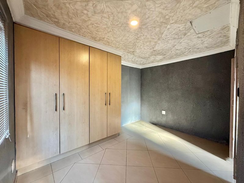 A vacant bedroom featuring built-in wooden cupboards, tiled flooring, and a decorative textured ceiling with coving.