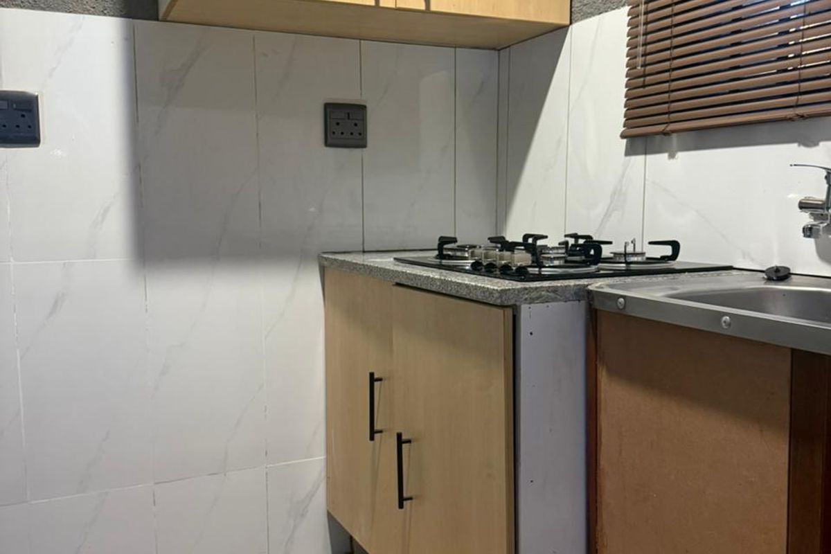 Compact kitchen area featuring light wood cabinetry, a built-in gas hob, stainless steel sink, and marble-effect wall tiling.