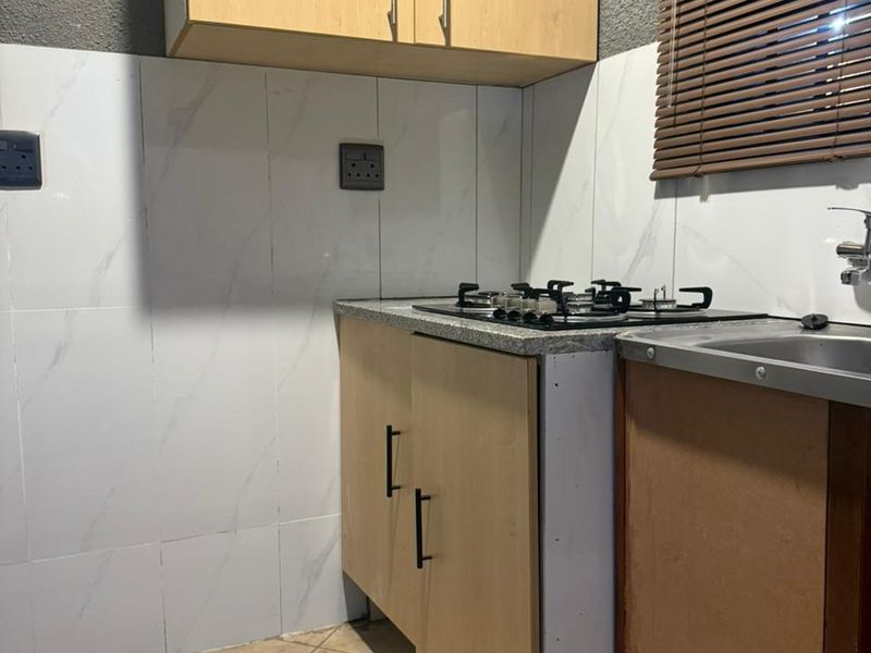 Compact kitchen area featuring light wood cabinetry, a built-in gas hob, stainless steel sink, and marble-effect wall tiling.