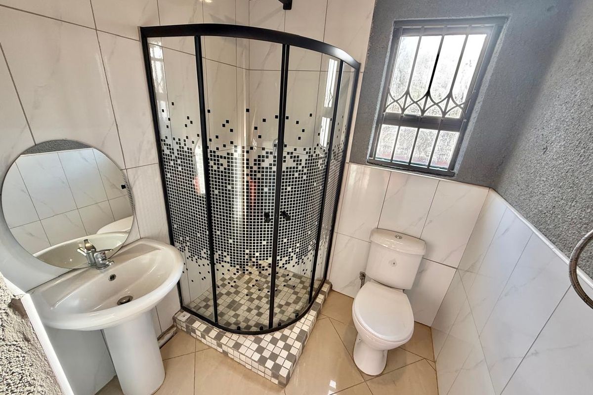 A modern bathroom featuring a corner shower enclosure, pedestal basin, and toilet with white tiled walls and neutral floor tiles.