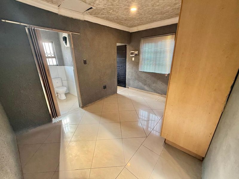 A bedroom featuring tiled flooring, a built-in cupboard, and an en-suite bathroom, requiring cosmetic updates to the wall finishes and ceiling.