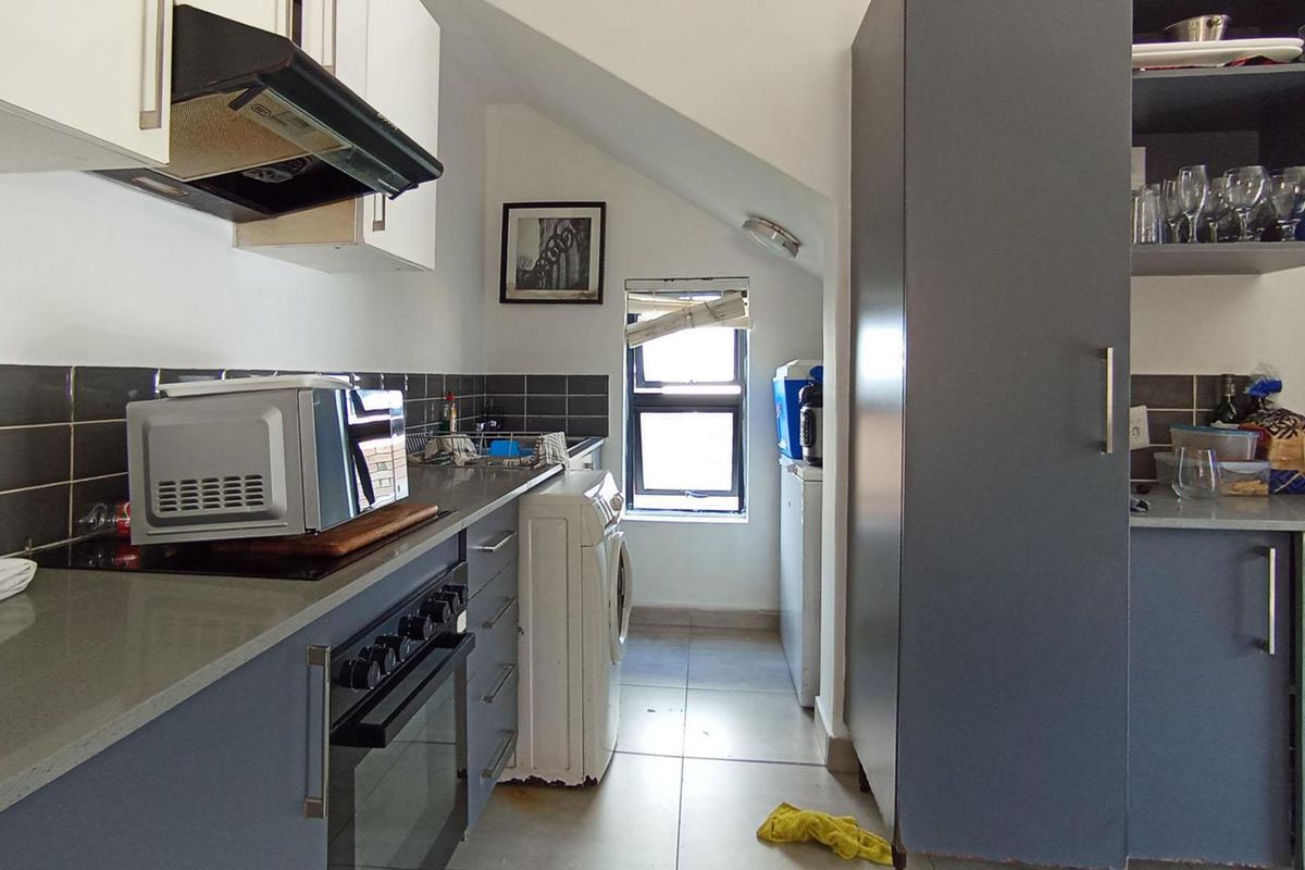 Compact kitchen featuring built-in cabinetry, stone countertops, tiled backsplash, and integrated oven with extractor fan, situated under a sloped ceiling.