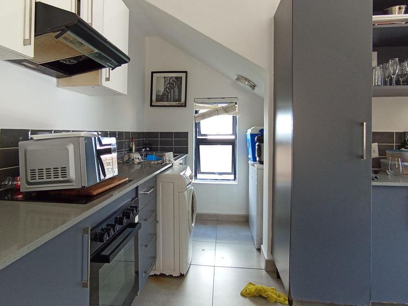 Compact kitchen featuring built-in cabinetry, stone countertops, tiled backsplash, and integrated oven with extractor fan, situated under a sloped ceiling.