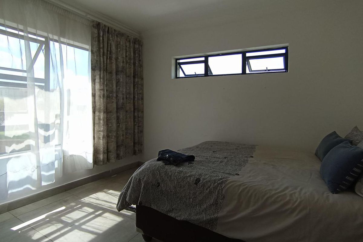 A bedroom featuring tiled flooring, a large window with natural light, and a high-level clerestory window for additional ventilation.