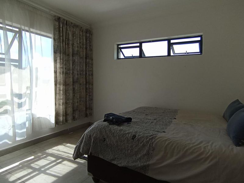 A bedroom featuring tiled flooring, a large window with natural light, and a high-level clerestory window for additional ventilation.