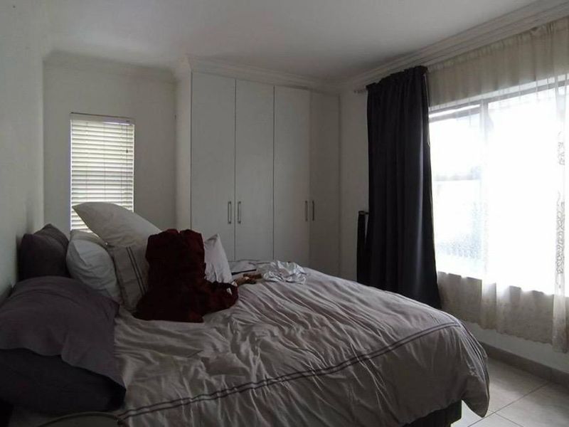 A bedroom featuring built-in cupboards, tiled flooring, and decorative cornice detailing, offering a functional space with natural light.
