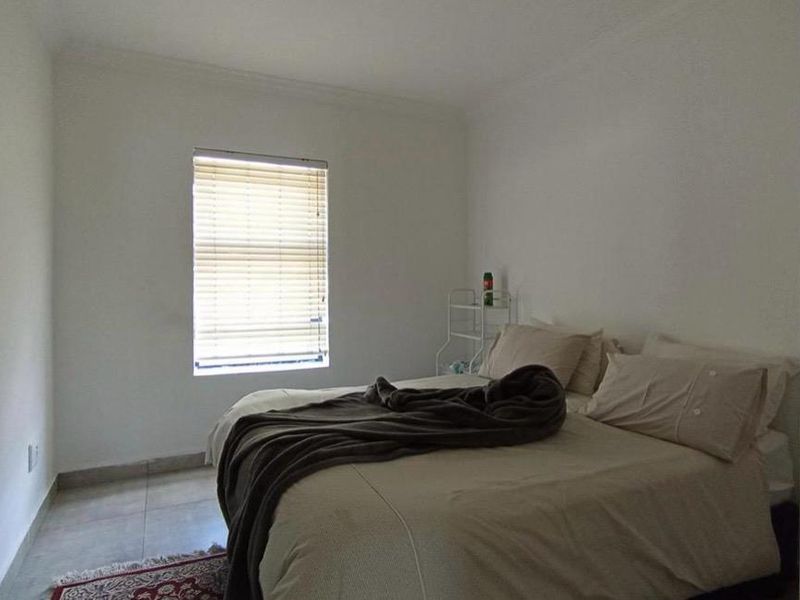 A simple bedroom featuring tiled flooring and a window fitted with venetian blinds, offering a neutral space ready for personalization.