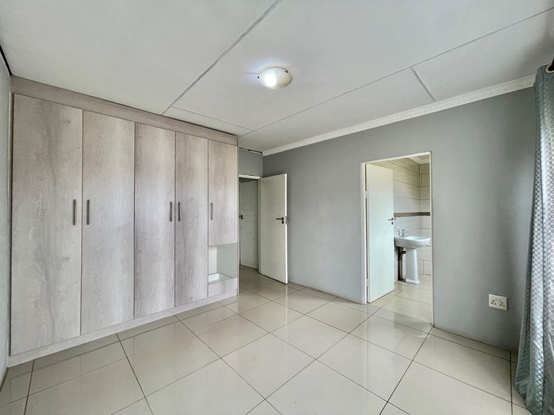 A spacious bedroom featuring built-in cupboards, tiled flooring, and direct access to an en-suite bathroom.