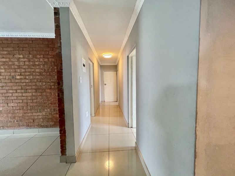 A bright hallway featuring tiled flooring, decorative ceiling cornices, and an exposed brick feature wall, leading to multiple interior rooms.