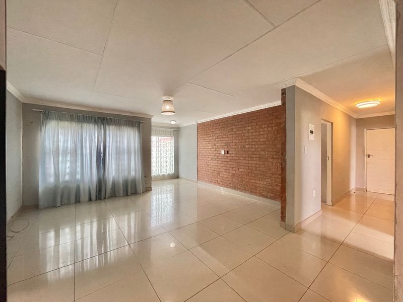 Spacious living area featuring polished tile flooring, a prominent exposed brick feature wall, and neutral finishes throughout.