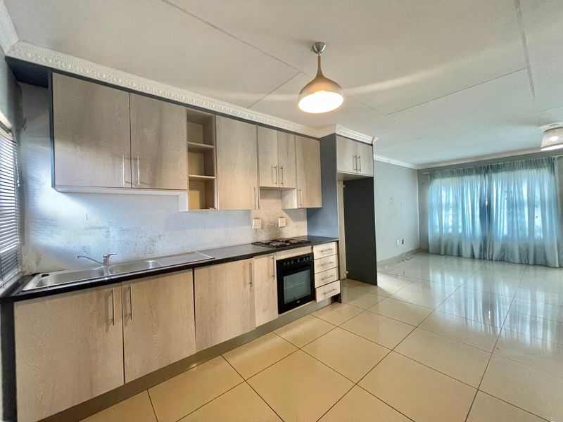 Open-plan kitchen and living area featuring light wood-finish cabinetry, tiled flooring, and integrated appliances, offering a clean and functional layout.