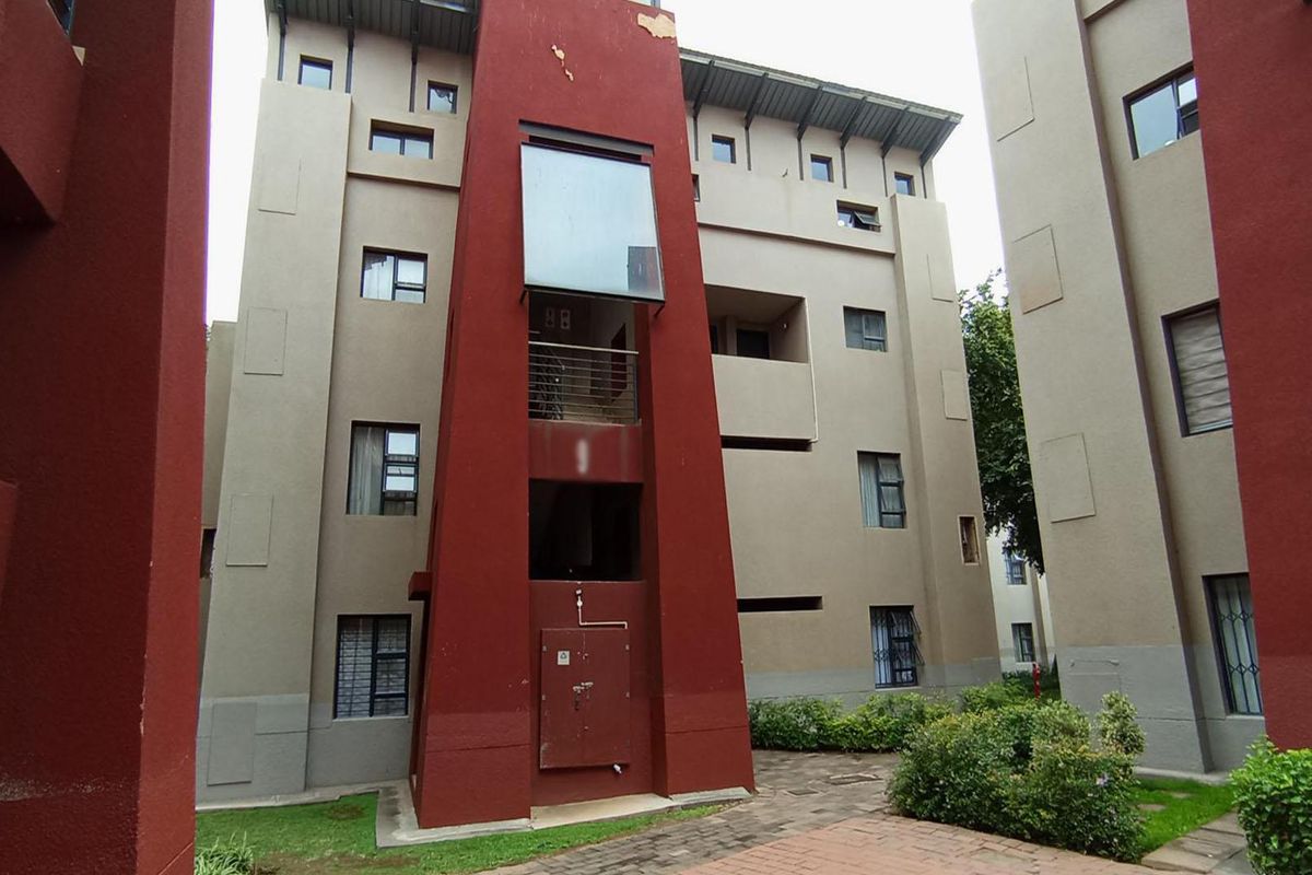 Exterior view of a multi-story apartment complex featuring a red and beige facade with balconies and surrounding landscaped garden areas.
