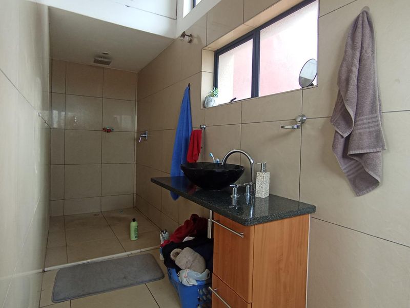 A functional bathroom featuring a walk-in shower, granite-topped vanity with a vessel sink, and neutral wall tiling.