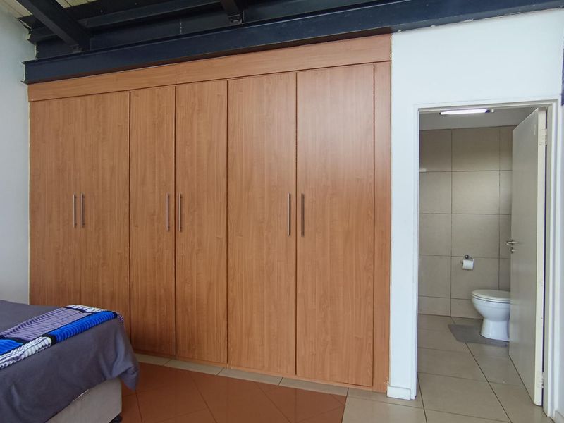 Bedroom featuring extensive built-in wooden cupboards, exposed industrial-style steel ceiling beams, and direct access to an en-suite bathroom.