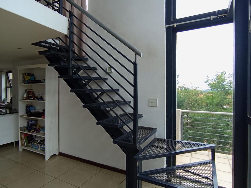 Open plan living area featuring a modern metal staircase leading to a mezzanine level, with large glass doors opening onto a balcony.