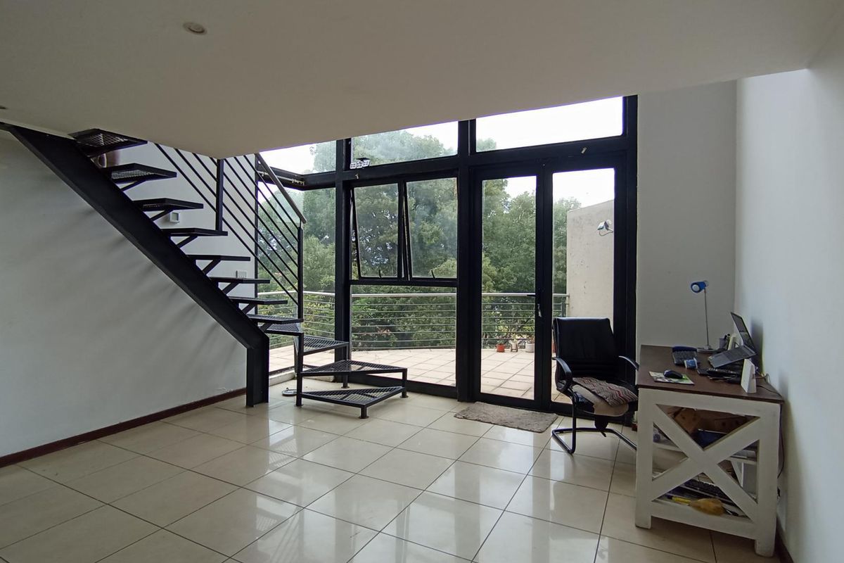 Spacious living area featuring a modern metal staircase, large glass doors leading to a balcony, and neutral tiled flooring throughout.