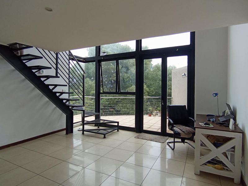 Spacious living area featuring a modern metal staircase, large glass doors leading to a balcony, and neutral tiled flooring throughout.