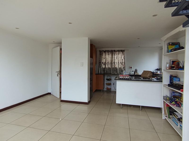 Open-plan living area featuring tiled flooring, recessed lighting, and a functional kitchen island with built-in cabinetry, leading to an upper level via a staircase.