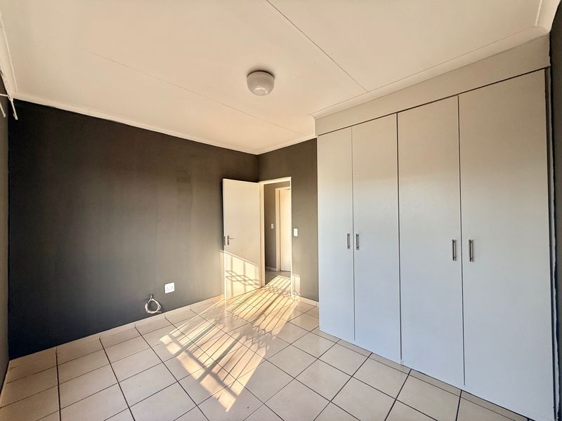 An empty bedroom featuring tiled flooring, built-in cupboards, and a neutral color scheme with a dark accent wall.