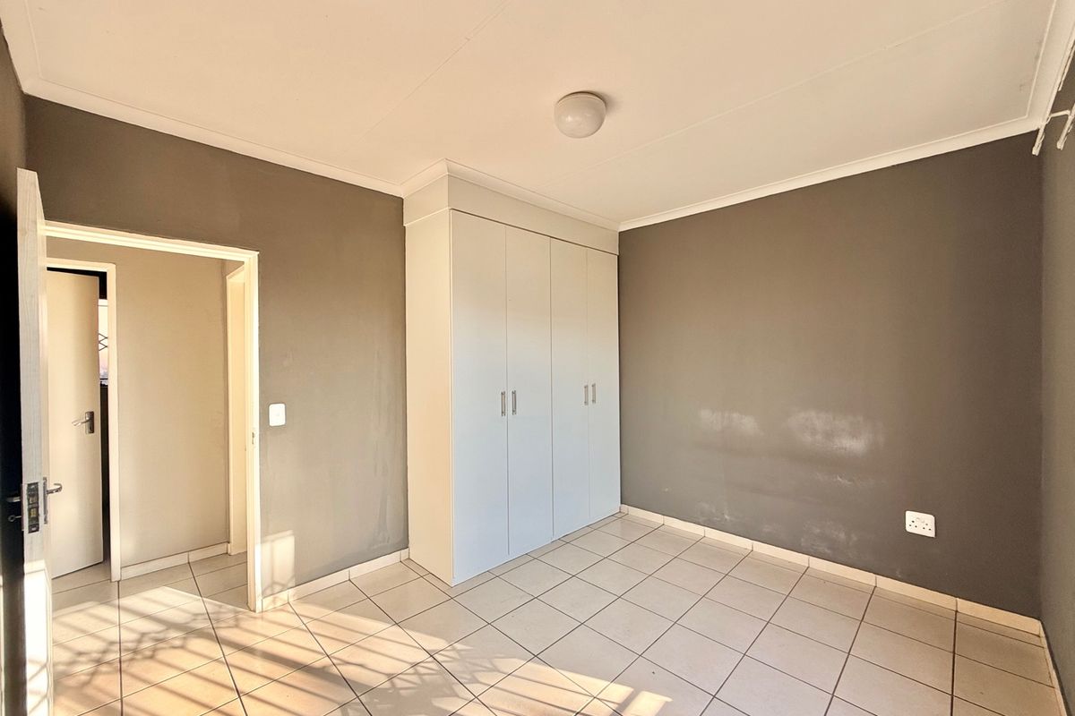 An empty bedroom featuring tiled flooring, a built-in wardrobe, and neutral grey walls, offering a blank canvas for personalization.