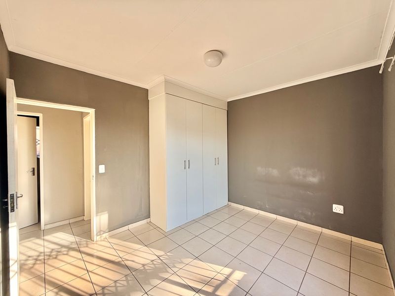 An empty bedroom featuring tiled flooring, a built-in wardrobe, and neutral grey walls, offering a blank canvas for personalization.