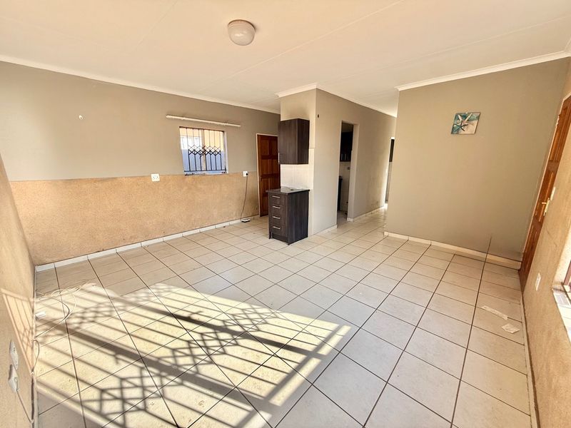 An open-plan living area featuring tiled flooring, security gates on windows, and basic built-in cabinetry, offering a blank canvas for renovation.